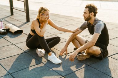 Genç bir adam ve kadın dışarıda spor yaparken konuşuyorlar.