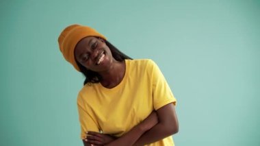 Gülen Afrikalı kadın el ele tutuşup turkuaz stüdyodaki kameraya bakıyor.