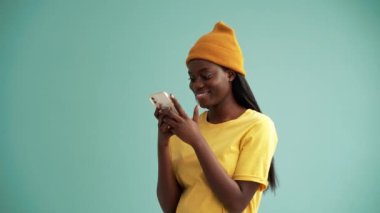 Turkuaz stüdyoda telefonla mesajlaşan güzel Afrikalı kadın.