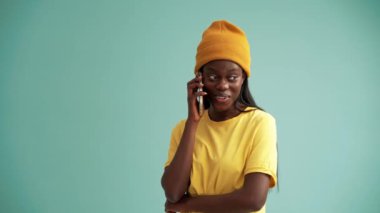 Turkuaz stüdyoda telefonla konuşan neşeli Afrikalı kadın.