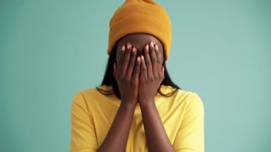 Turkuaz stüdyoda saklambaç oynayan gülümseyen Afrikalı kadın.