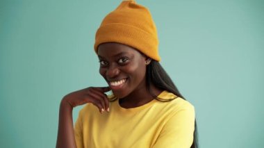 Turkuaz stüdyoda gülümseyen Afrikalı kadın kameraya poz veriyor.