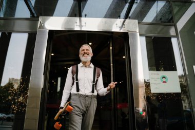 Gri, olgun bir adam dışarıda kaykay yaparken gülümsüyor.