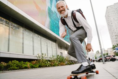 Şehrin sokaklarında kaykay yaparken sakallı, olgun bir adam gülümsüyor.