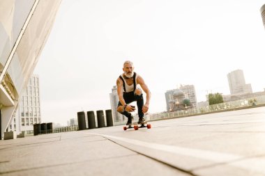 Dışarıda park yerinde sakallı kaykaylı gri olgun bir adam.