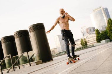 Dışarıdaki otoparkta sakallı kaykaycı gömleksiz olgun bir adam.