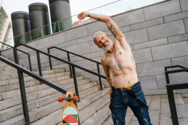 Yetişkin beyaz tişörtsüz adam gülümsüyor ve dışarıda spor yapıyor.