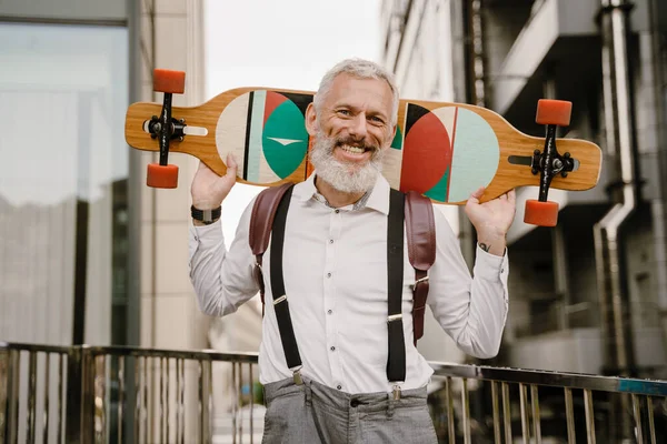 灰色成熟男子笑着站在城市街道上的滑板上 — 图库照片