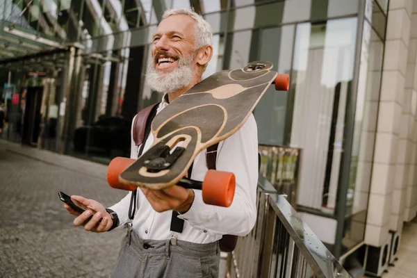 Grigio Uomo Maturo Utilizzando Cellulare Mentre Piedi Con Skateboard Città — Foto Stock