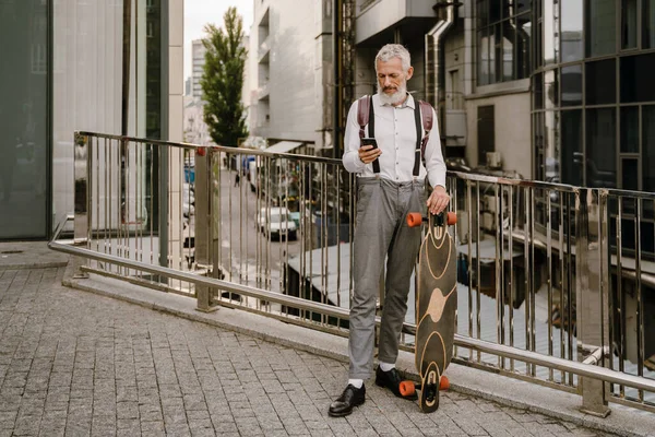 Grey Starší Muž Pomocí Mobilu Zatímco Stojí Skateboard Ulici — Stock fotografie