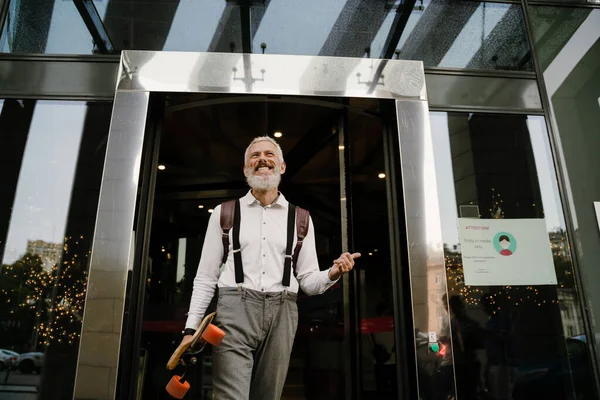 Gri, olgun bir adam dışarıda kaykay yaparken gülümsüyor.