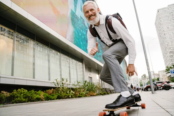 Şehrin sokaklarında kaykay yaparken sakallı, olgun bir adam gülümsüyor.