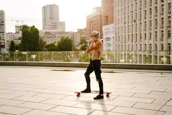 Zralý Muž Bez Trička Poslouchá Hudbu Sluchátky Při Skateboardingu Parkovišti — Stock fotografie