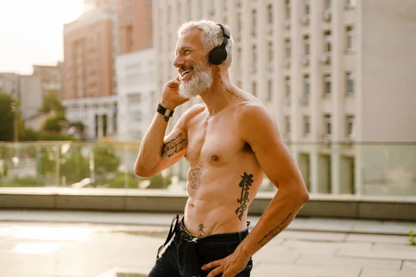Shirtless Mature Man Listening Music Headphones While Standing Outdoors — стоковое фото