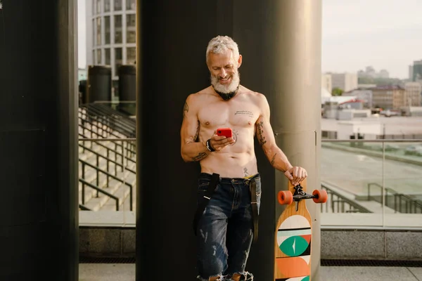 Shirtless Mature Man Using Cellphone While Standing Skateboard City Street — Foto Stock