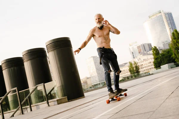 Dışarıdaki otoparkta sakallı kaykaycı gömleksiz olgun bir adam.