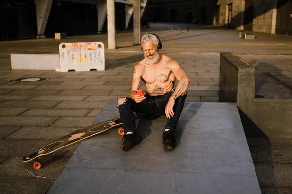 Uomo Maturo Shirtless Utilizzando Telefono Cellulare Mentre Seduto Con Skateboard — Foto Stock