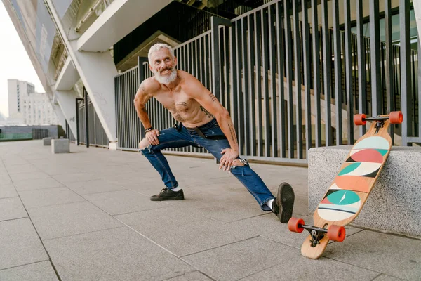 Yetişkin beyaz tişörtsüz adam dışarıda kaykayıyla antrenman yapıyor.