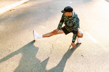 Genç sporcu dışarıda şehir yolunda çalışırken egzersiz yapıyor.