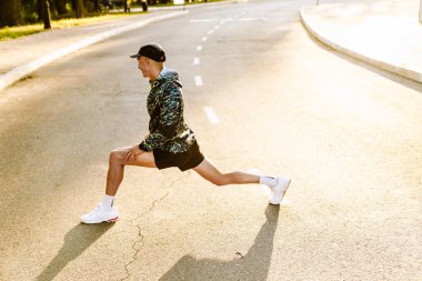 Genç sporcu dışarıda şehir yolunda çalışırken egzersiz yapıyor.