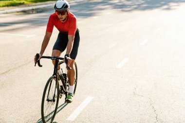 Kasklı genç sporcu dışarıda çalışırken yarış bisikleti sürüyor.