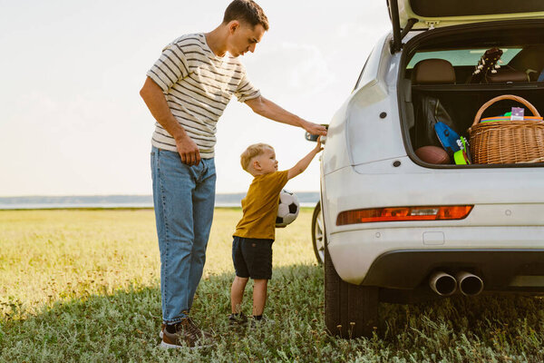 Young white father and his small son standing by car while playing outdoors