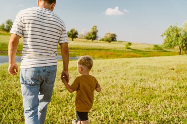 Genç beyaz baba çizgili tişört giyiyor ve yaz tarlasında oğluyla yürüyor.