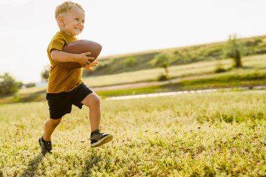 Sarışın beyaz çocuk dışarıda rugby oynarken gülümsüyor.