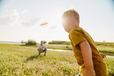 Genç beyaz baba ve oğlu dışarıda frizbi oynuyorlar.