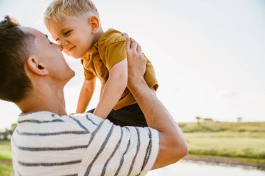 Genç beyaz bir baba çizgili tişört giyiyor ve oğlunu dışarıda tutuyor.