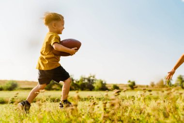Sarışın beyaz çocuk dışarıda rugby oynarken gülümsüyor.