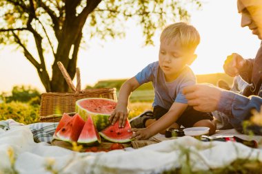 Genç beyaz baba ve oğul yaz tarlasında piknik yaparken karpuz yiyorlar.
