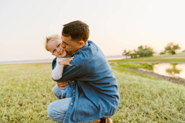 Genç beyaz baba yaz tarlasında oğlunu öpüyor ve sarılıyor.