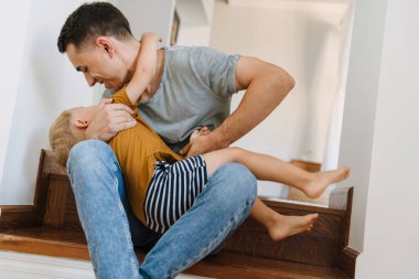 Genç beyaz baba evdeki merdivenlerde oğluyla dalga geçiyor.