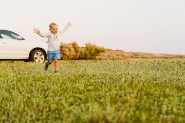Sarışın beyaz çocuk, yaz tarlasında koşarken gülümsüyor.