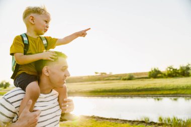 Küçük oğlunu omuzlarında taşırken el kol hareketi yapan genç bir baba.