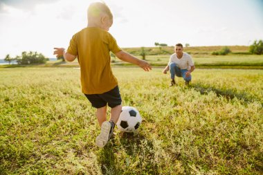 Genç beyaz baba ve küçük oğlu dışarıda futbol oynuyorlar.