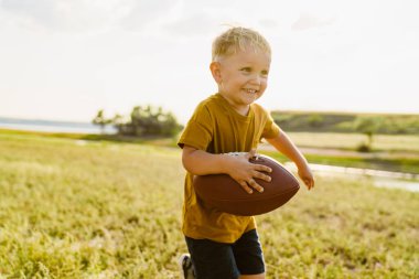 Sarışın beyaz çocuk dışarıda rugby oynarken gülümsüyor.