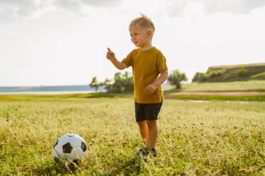 Dışarıda futbol oynarken gülümseyen sarışın küçük beyaz çocuk.