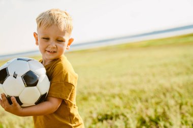 Dışarıda futbol oynarken gülümseyen sarışın beyaz çocuk.