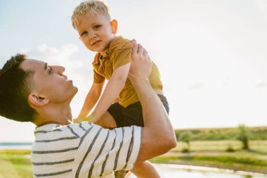 Genç beyaz bir baba çizgili tişört giyiyor ve oğlunu dışarıda tutuyor.