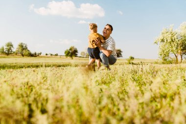 Genç beyaz baba dışarıda oğluyla oynuyor ve onunla dalga geçiyor.
