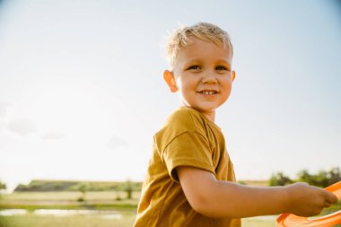 Sarışın beyaz çocuk dışarıda frizbi oynarken gülüyor.