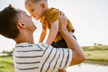 Genç beyaz bir baba çizgili tişört giyiyor ve oğlunu dışarıda tutuyor.