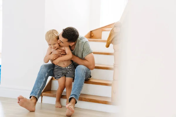 年轻的白人父亲在家里的楼梯上亲吻和拥抱他的儿子 — 图库照片