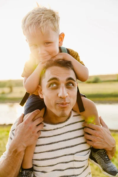 屋外に歩いている間に彼の肩の上に小さな息子を運ぶ若い白い父 — ストック写真