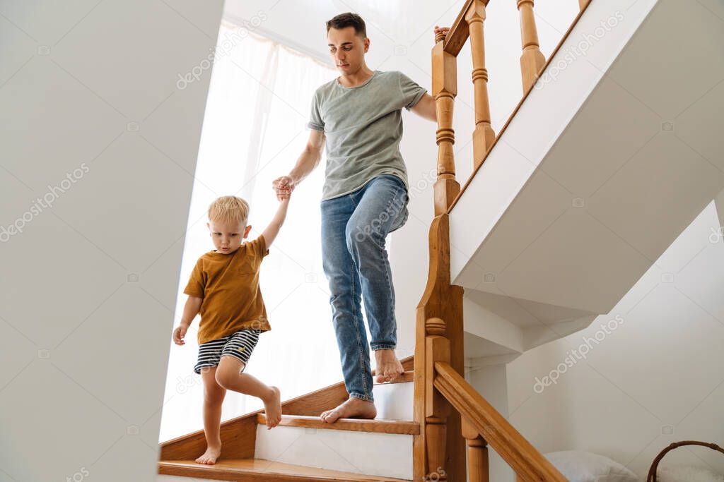 Young white father going down stairs with his son at home
