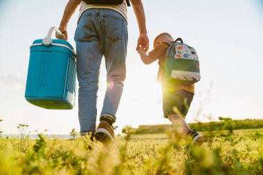 Genç beyaz baba ve oğul yaz tarlasında çantalarla yürüyorlar.