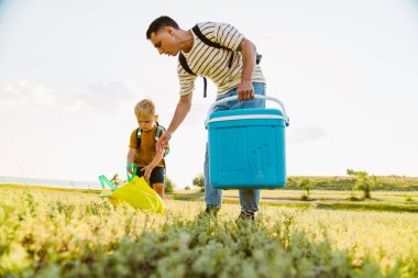 Genç beyaz baba ve oğul yaz tarlasında çantalarla yürüyorlar.