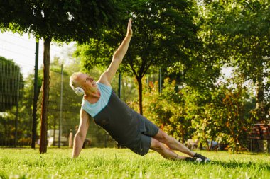 Yeşil Park 'taki yoga antrenmanında müzik dinleyen yaşlı gri sporcu.